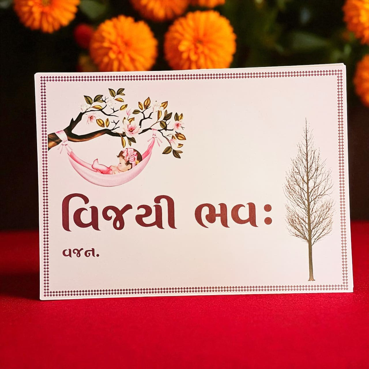 Card with illustrations of a baby in a hammock and a tree, on a red background with orange flowers.
